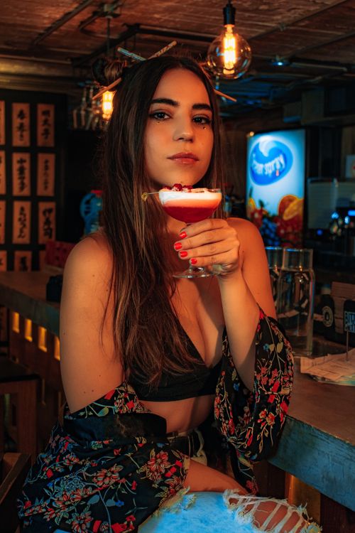 Free Elegant woman in fashionable attire sipping a cocktail at a vibrant nightclub bar. Stock Photo