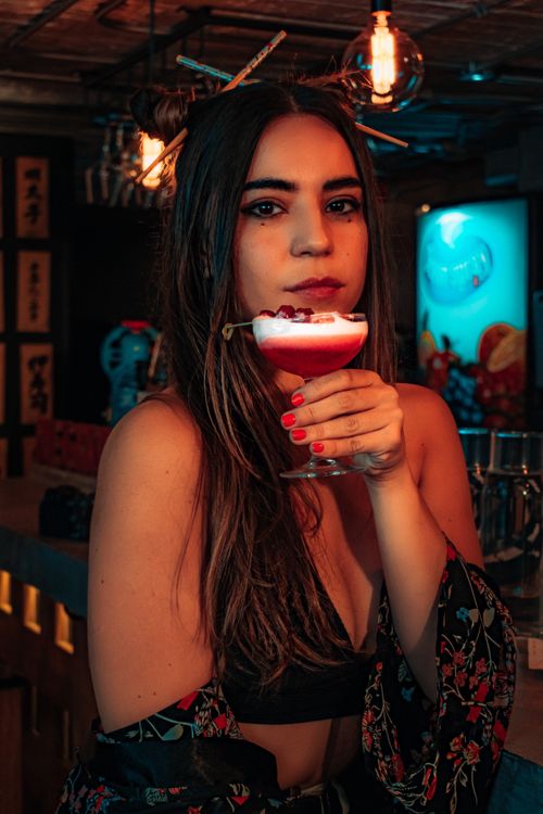Free A stylish woman enjoying a cocktail in a dimly lit nightclub setting. Stock Photo