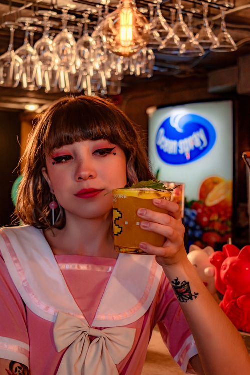 Free Stylish young woman with edgy makeup holding a cocktail in a modern bar setting. Stock Photo