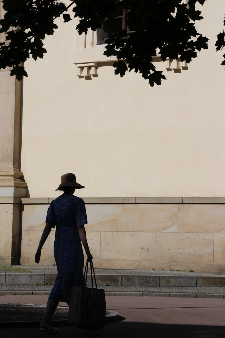 A Woman In A Dress Carrying A Bag While Walking