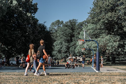 Teens enjoy a sunny day playing basketball at an outdoor court in a lush park.