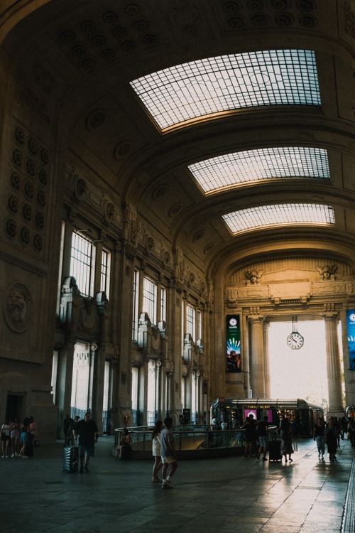 Free Dramatic view of a grand railway station interior with high ceilings and skylights, capturing people walking. Stock Photo