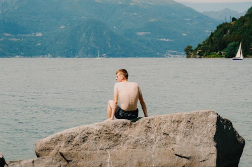 A Shirtless Man Sitting on the Rock Near the Sea