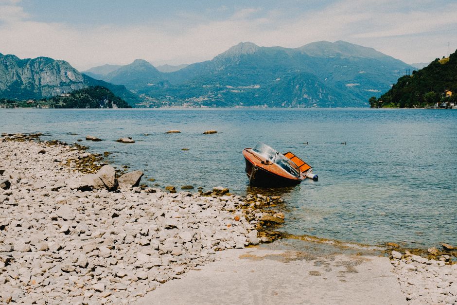 A tranquil lakeside scene with a boat, pebbled shore, and mountain backdrop.