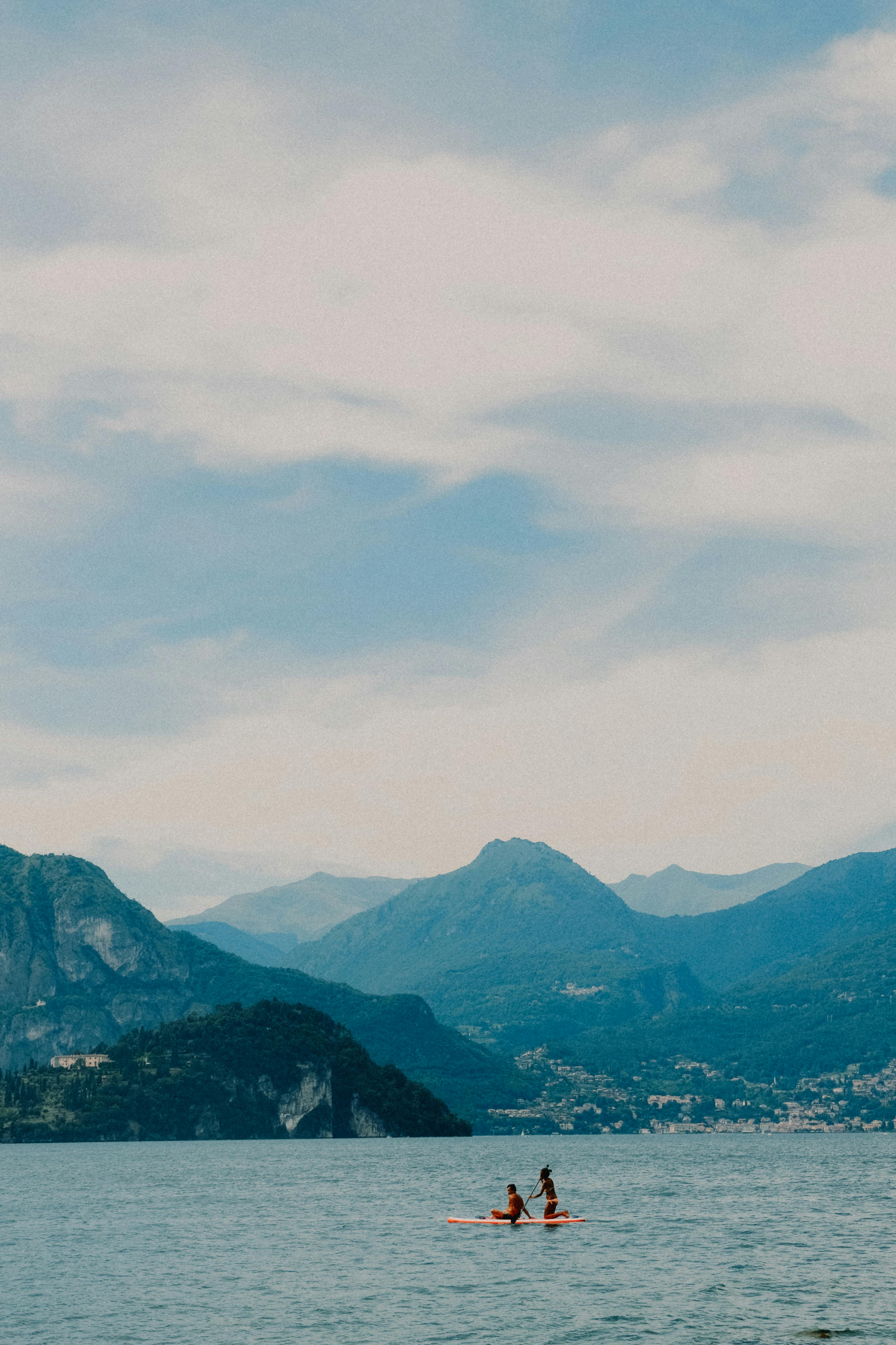 Tranquil scene of a lake with people paddleboarding and mountain views under a cloudy sky.