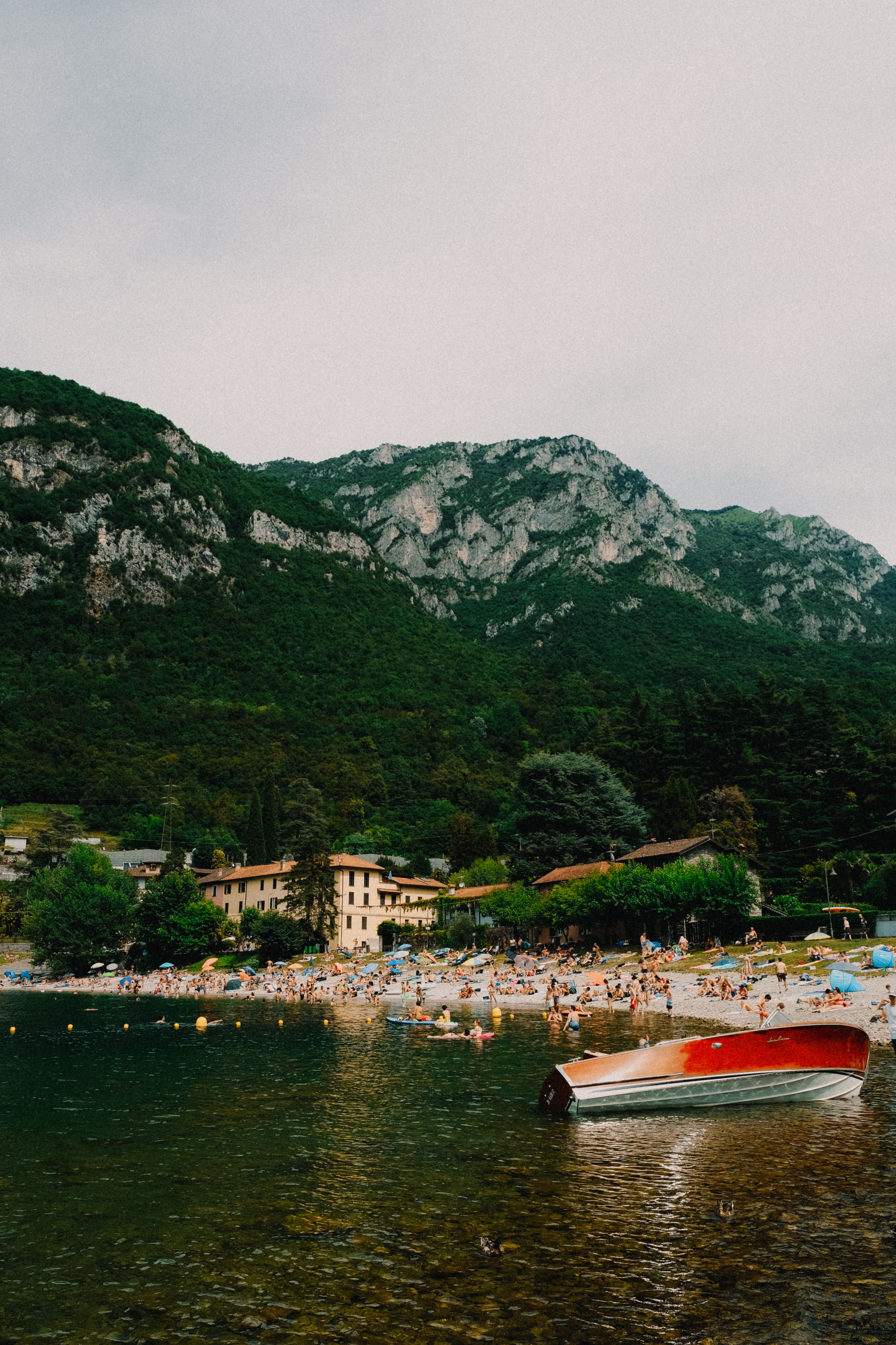 Crowded beach along a serene mountain lake in summer.
