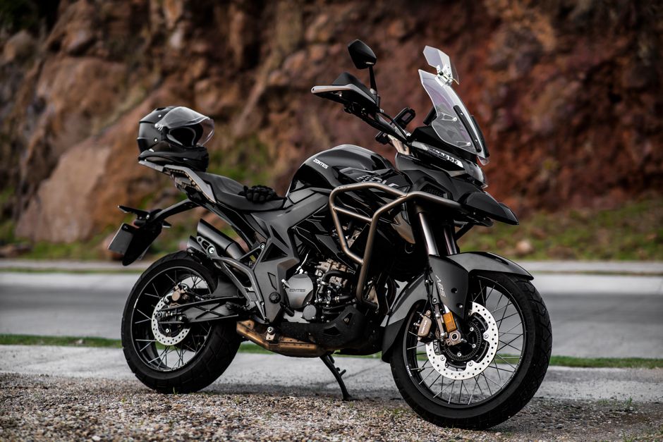 A modern adventure motorcycle parked on a scenic road with rocky terrain in the background.