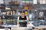 Woman working in a commercial kitchen surrounded by spices and machinery, focusing on her task.