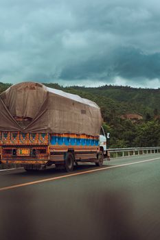 A vibrant truck travels on a road with lush greenery and cloudy skies, conveying a sense of journey.