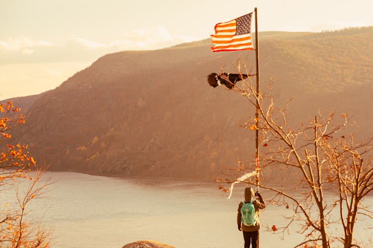 Man Holding A Flag Pole On Top Of A Mountain