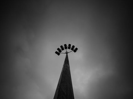Low-angle black and white shot of a towering stadium light pole against an overcast sky.