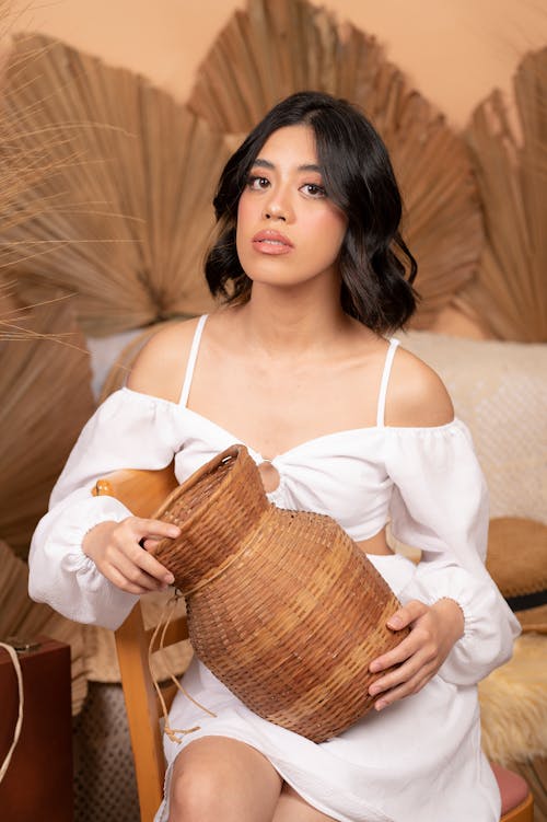 Woman Wearing a White Summer Dress Posing with a Wicker Basket and Dry Leaves Decoration