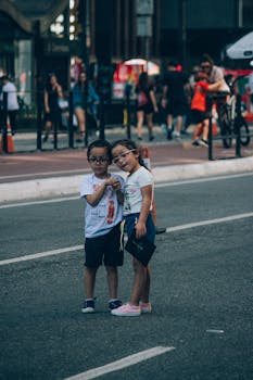 Adorable children holding hands on a busy urban street, surrounded by people.