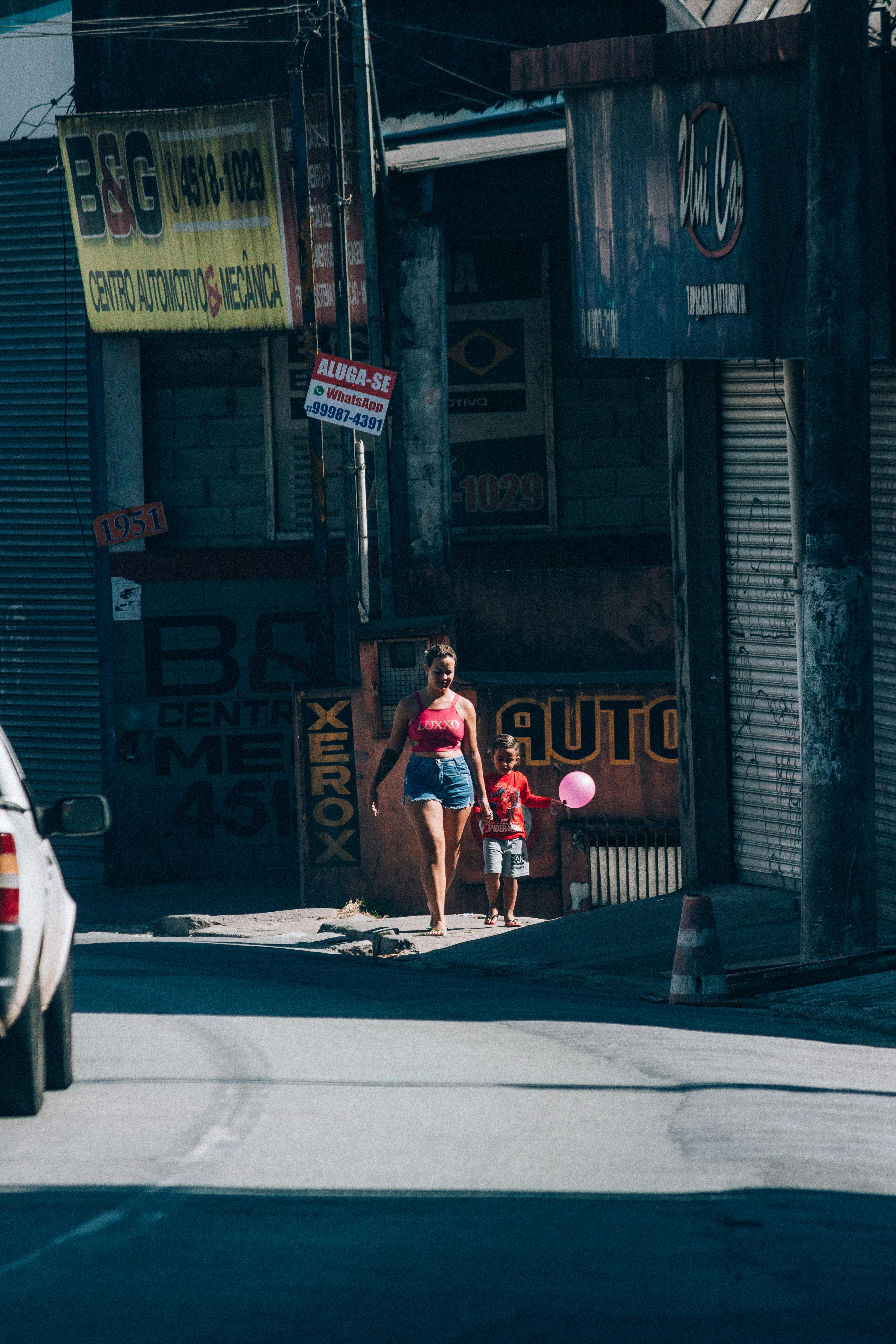 A woman and child walk on a sunny city street holding balloons.
