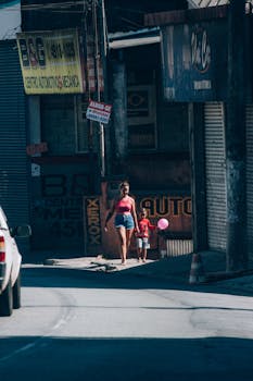 A woman and child walk on a sunny city street holding balloons.