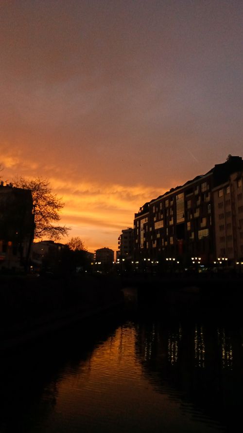 Free A stunning urban sunset reflecting on a canal with building silhouettes. Stock Photo