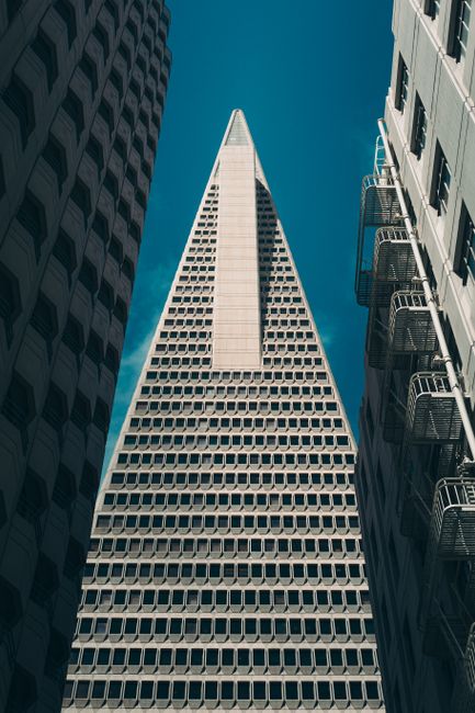 Vertical view of the iconic Transamerica Pyramid framed by surrounding buildings against a clear blue sky.