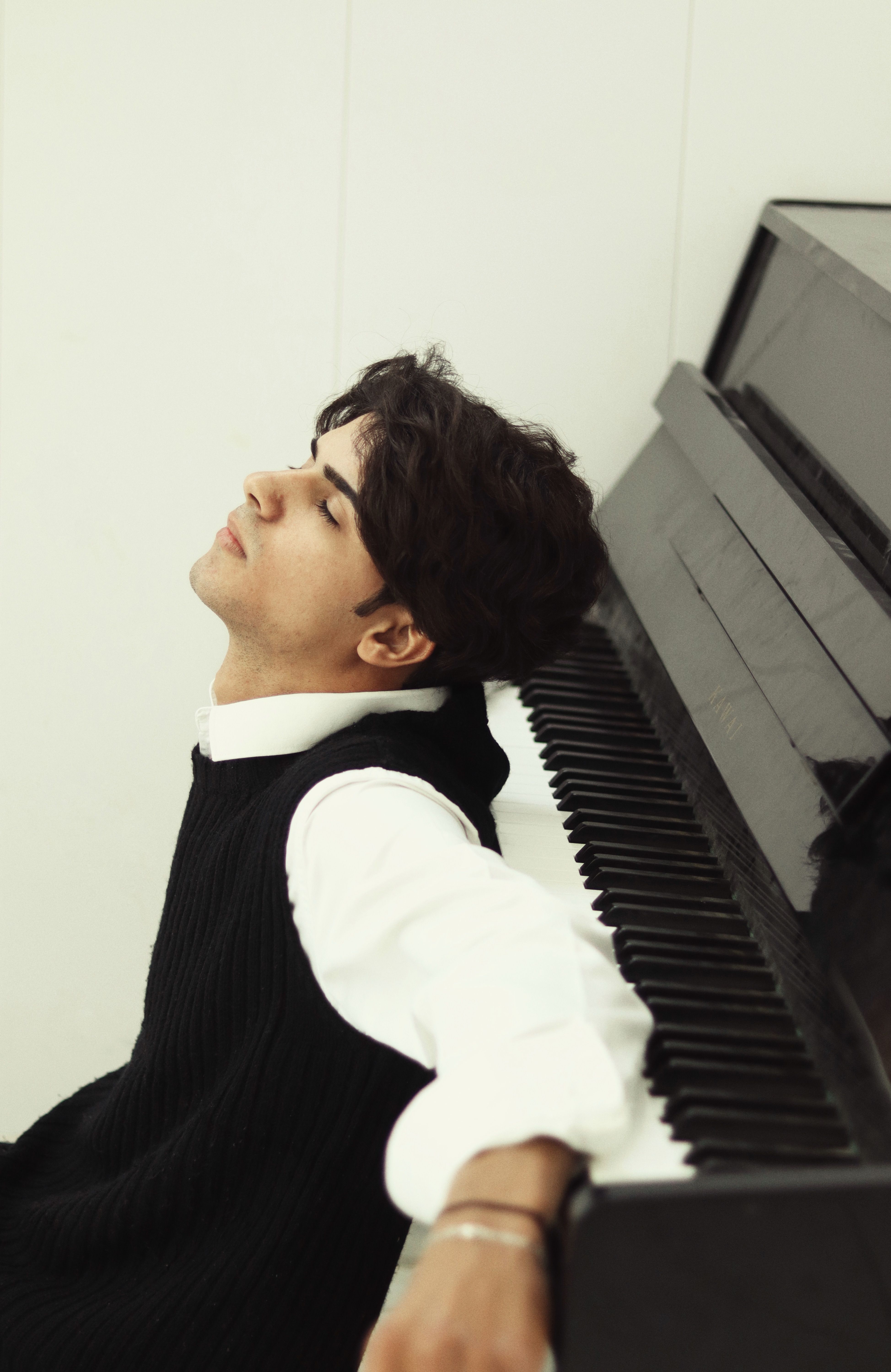A man rests against a black grand piano, embodying musical relaxation in a studio setting.
