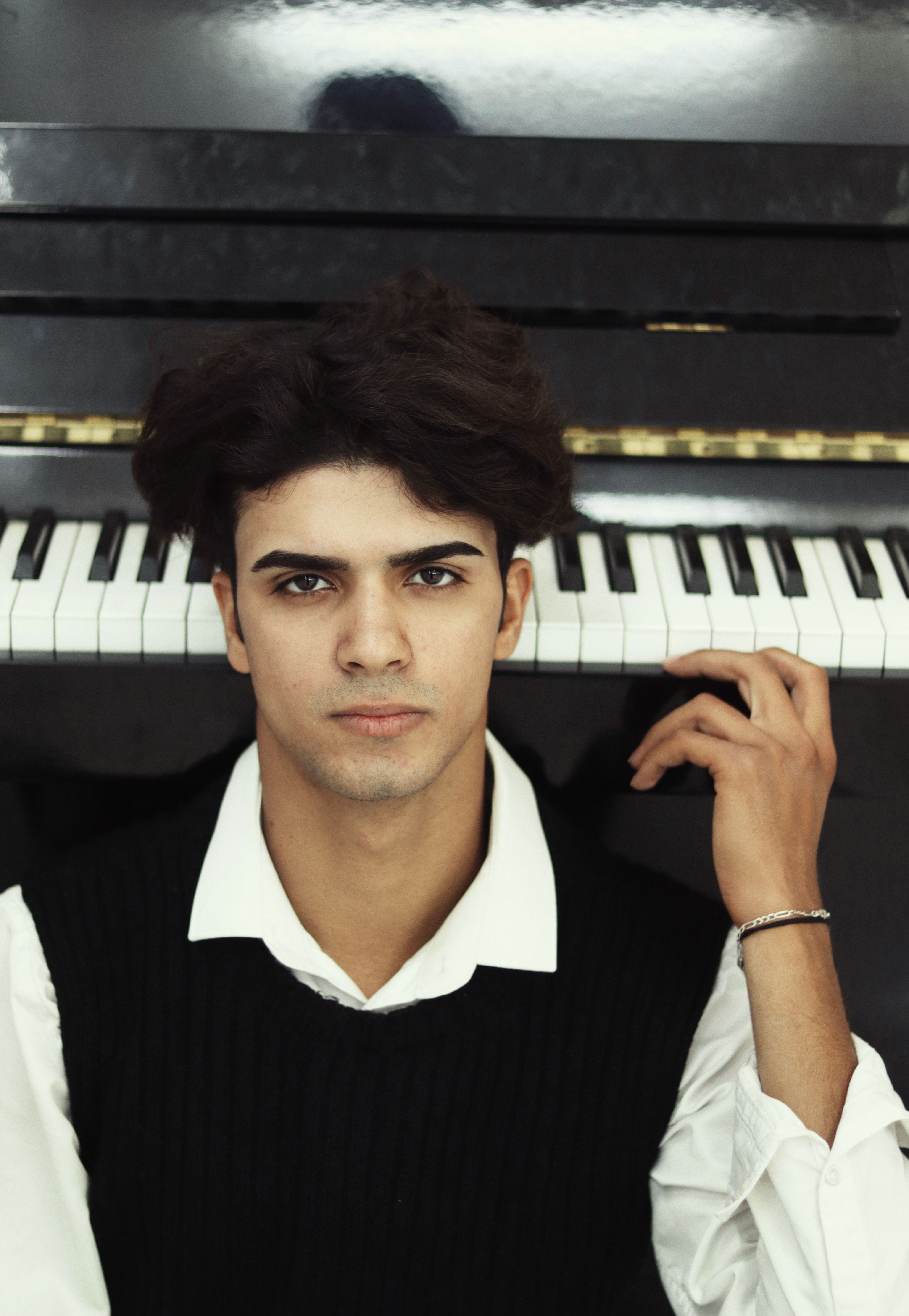 Portrait of a young man sitting in front of a piano, exuding calm confidence indoors.