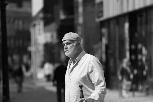Man Wearing Shirt and Cap Walking in Grayscale Photography