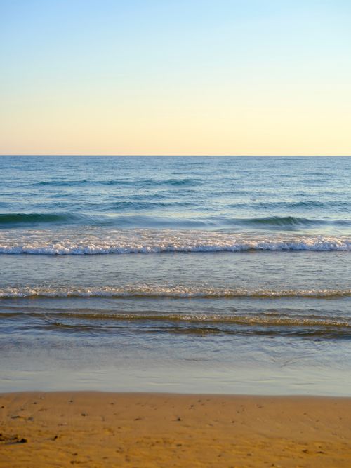 Free Tranquil view of ocean waves meeting the sandy shore at sunset on a deserted beach. Stock Photo