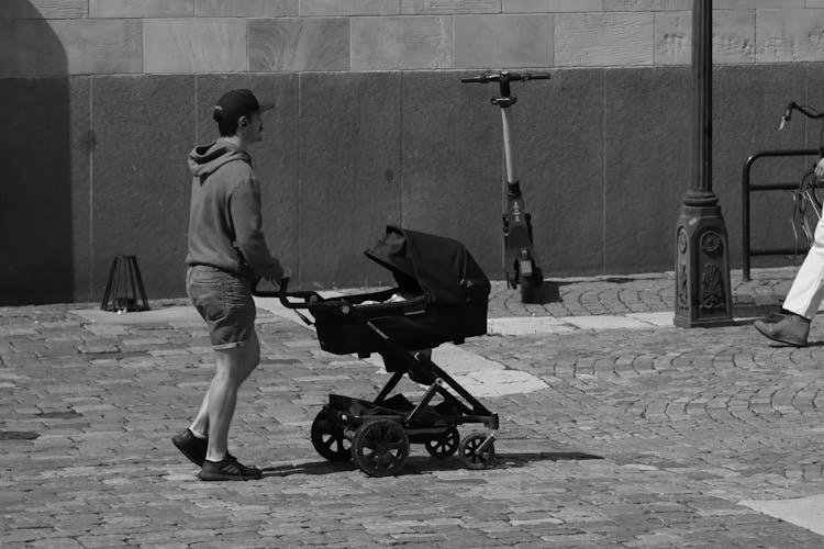 A Grayscale Of A Man Pushing A Baby Stroller