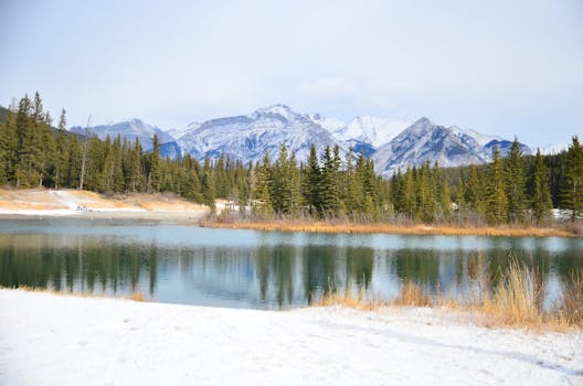 Tranquil winter scene of a snow-covered lake reflecting mountains and evergreen trees.