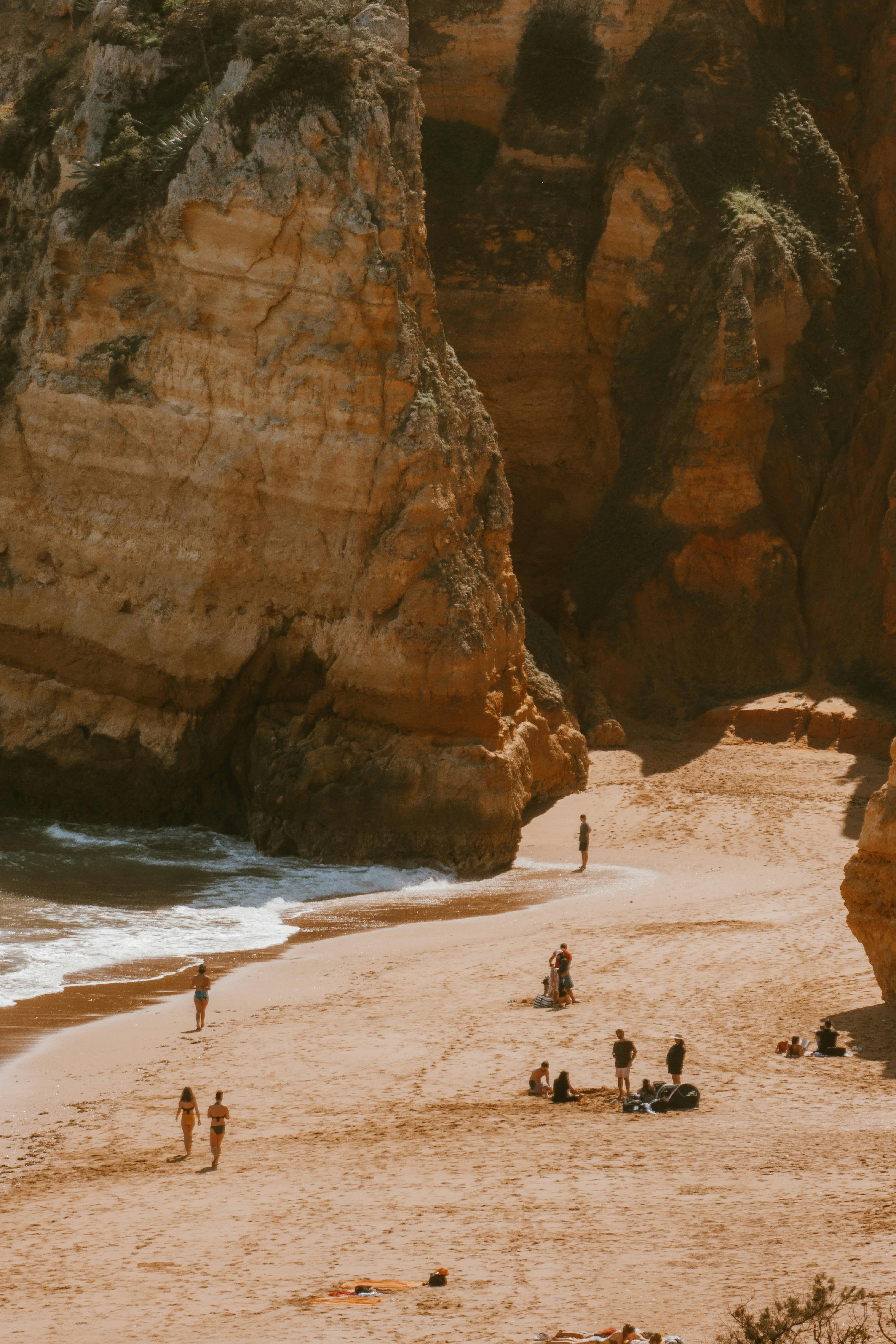 A picturesque beach scene with towering cliffs, people enjoying the sun, and waves gently hitting the shore.