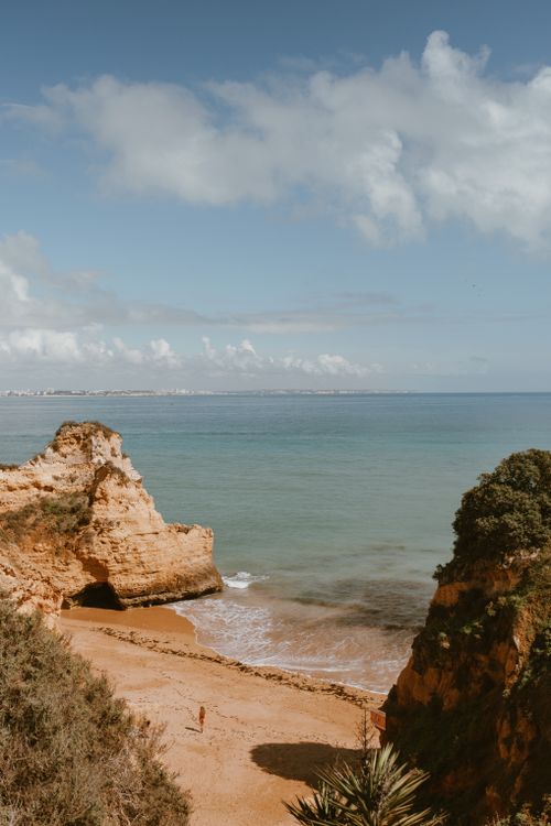 Free A serene beach scene with cliffs overlooking calm blue ocean under a bright summer sky. Stock Photo