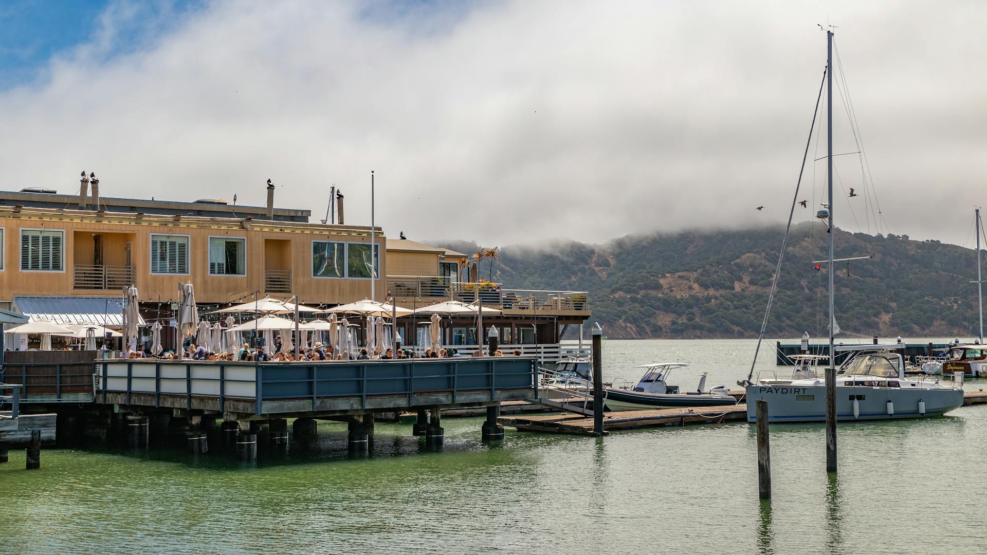 Charming waterfront restaurant with sailboats and hills in view, offering a relaxing dining experience.