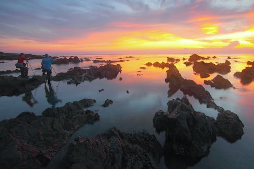 無料 日没時に水に映る岩層に立つ2人 写真素材