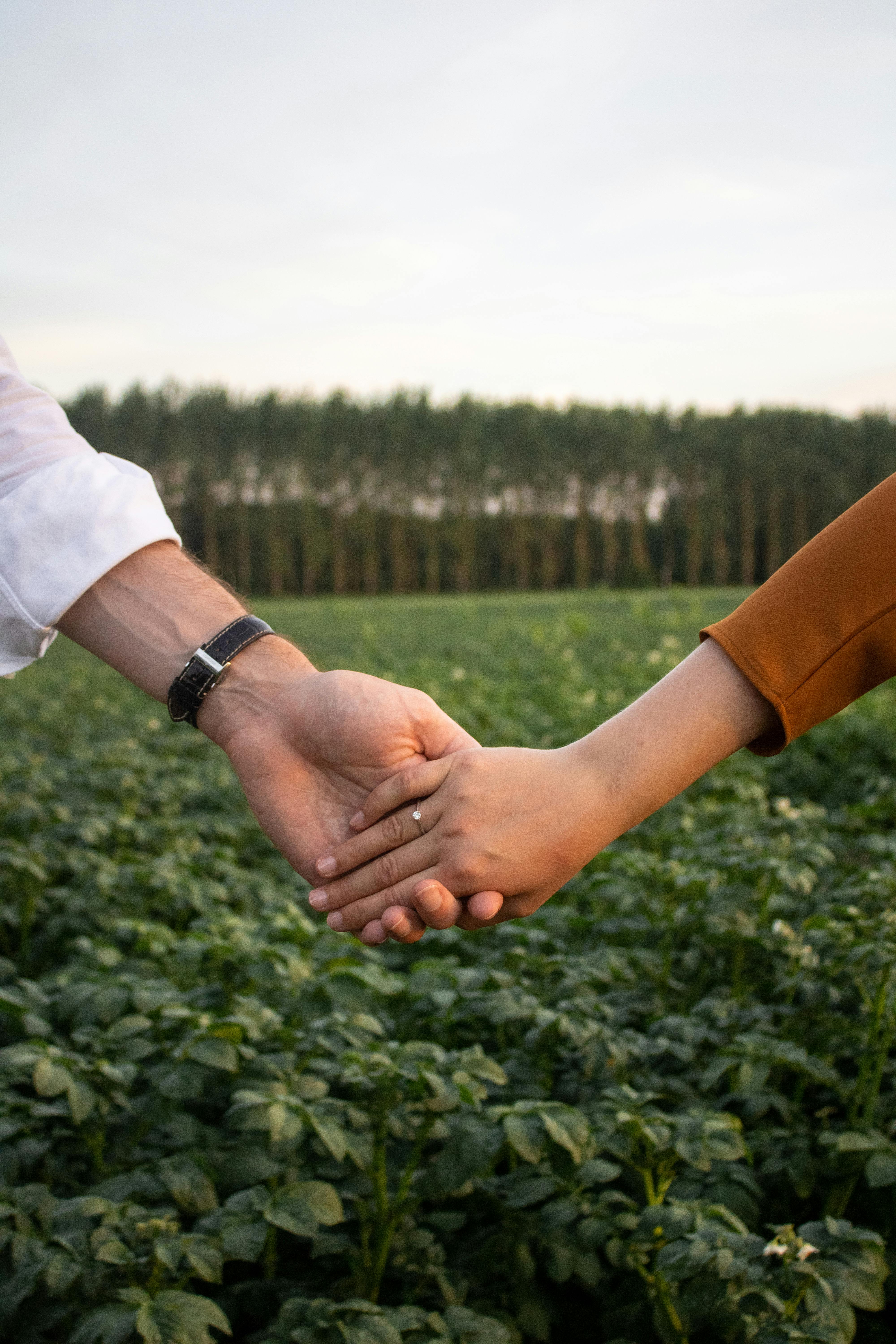 A couple holding hands outdoors amidst lush greenery, symbolizing love and connection.