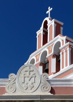 Ornate classic church architecture with bell tower and cross in Mesaria, Santorini.