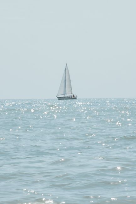 Peaceful sailboat on the ocean with shimmering water and clear sky.