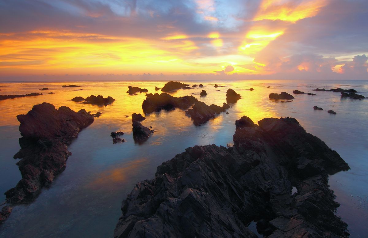 Sunrise over a rocky tidal shelf with still water between the rocks — photo by Pok Rie on Pexels
