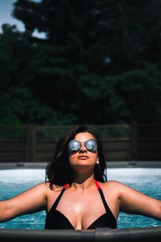 A woman in sunglasses relaxes in a pool under the summer sun, enjoying leisure and tranquility.