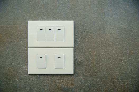 Minimalist photo of white electrical rocker switches on a textured stone wall background.