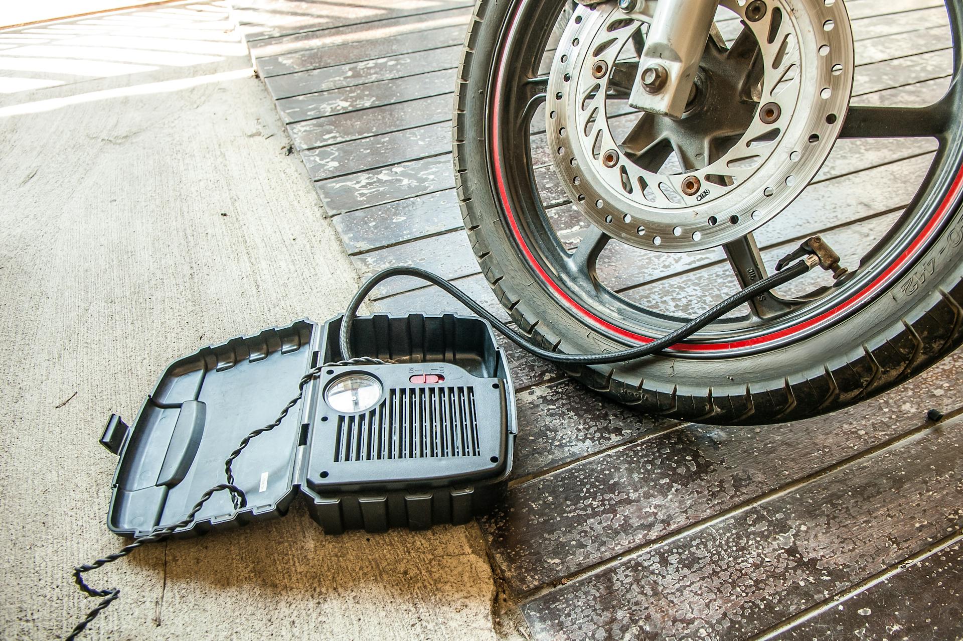 Close-up of a motorcycle tire being inflated using a portable air pump.
