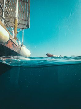 A unique view capturing half-above and half-below water with a sailboat and clear blue sky.