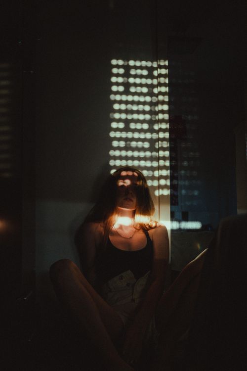 Free Artistic portrait of a woman sitting in a dark room with dramatic light patterns. Stock Photo