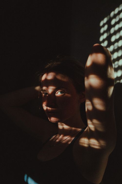 Free A woman in a black top with striking shadows across her face and arms, creating a dramatic and artistic portrait. Stock Photo