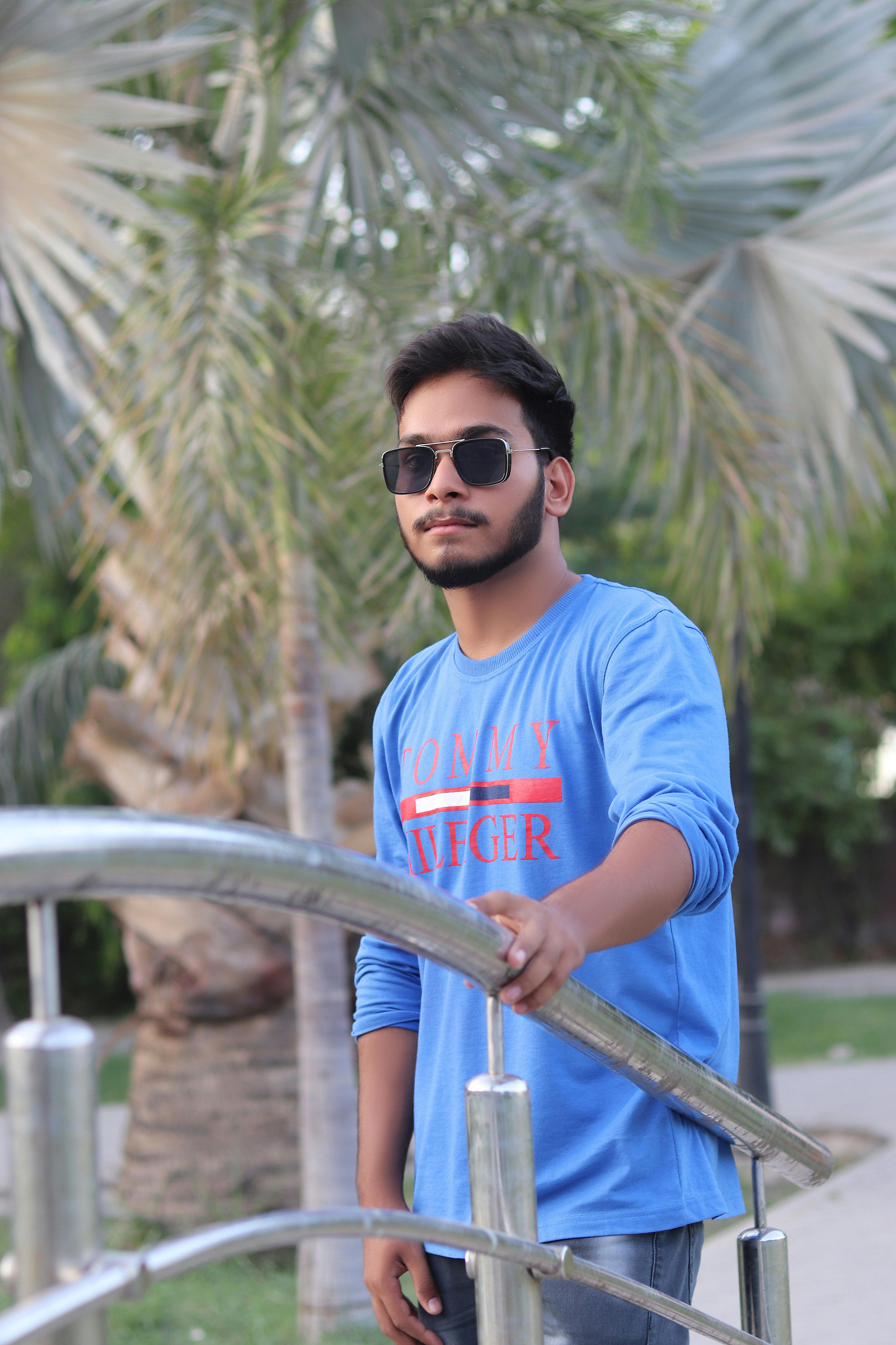 Portrait of an Asian man in sunglasses and blue sweater standing outdoors by a railing.
