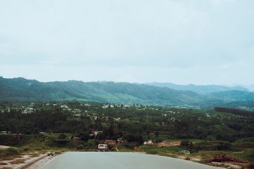 Free A serene mountain valley landscape featuring a road, lush greenery, and distant hills under a soft sky. Stock Photo