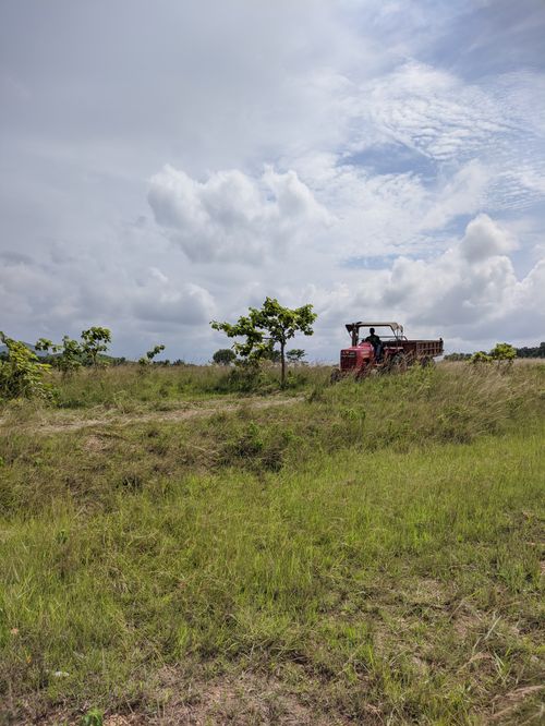 Free Tractor working in a lush farm field under a cloudy sky, capturing the essence of rural agriculture. Stock Photo