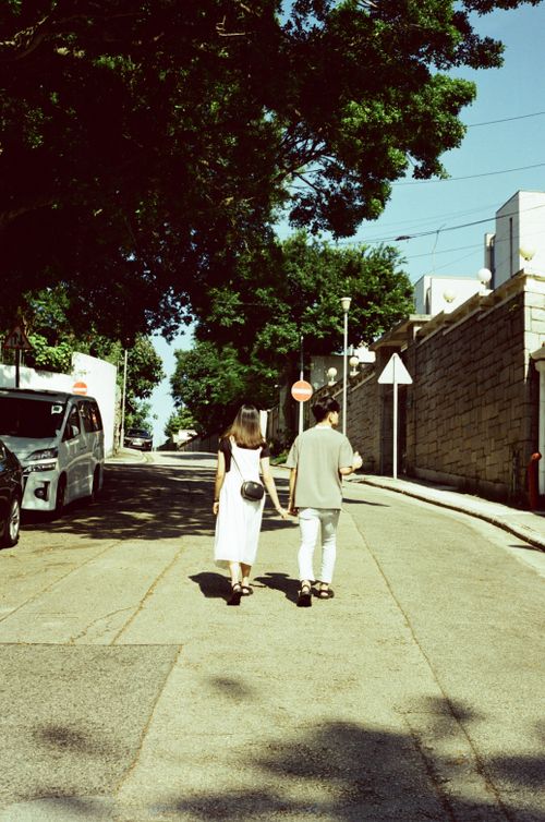 Free A couple strolls hand in hand down a quiet street in Hong Kong, under the shade of large trees. Stock Photo