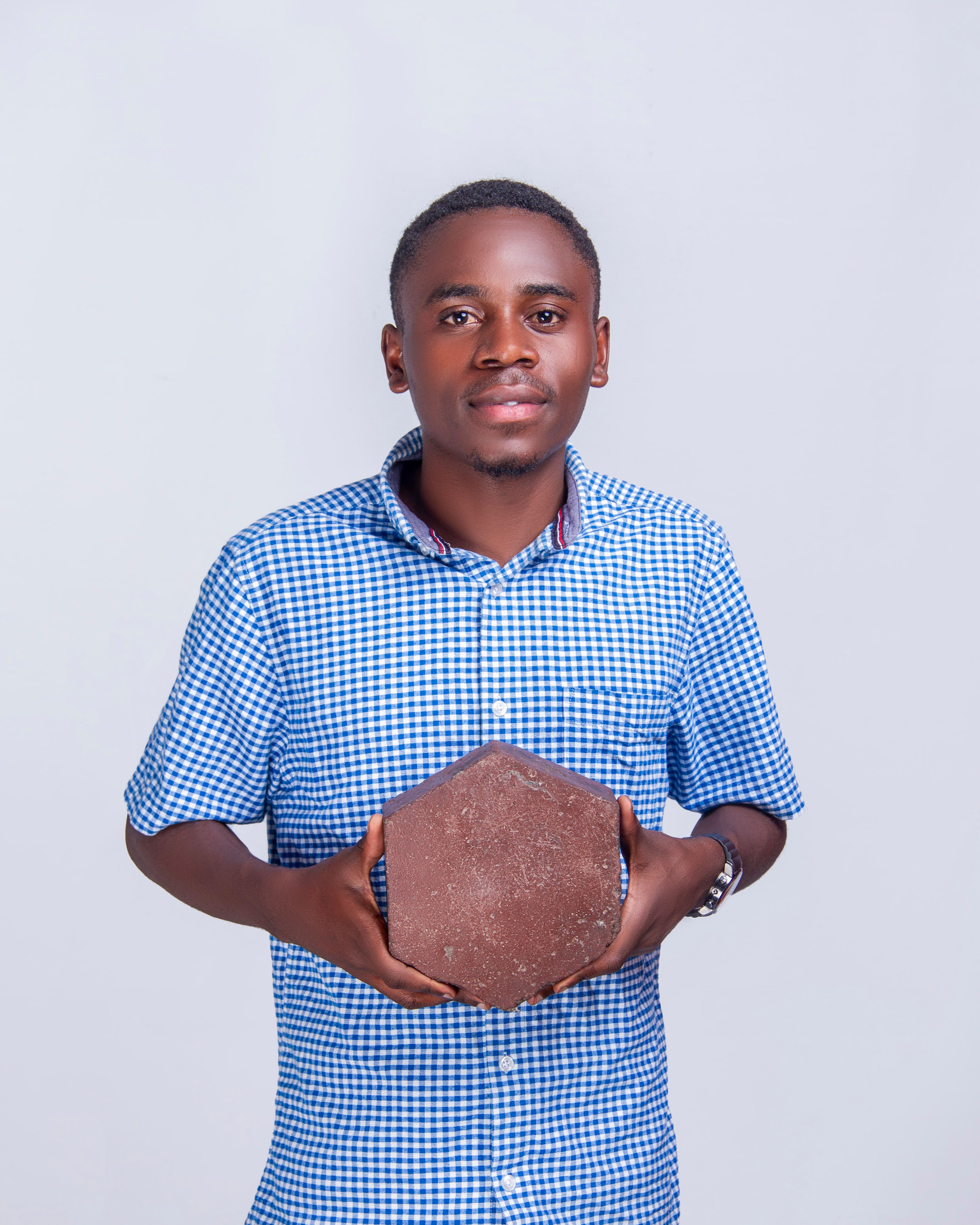 Portrait of an African man holding a hexagonal object against a plain white studio background.