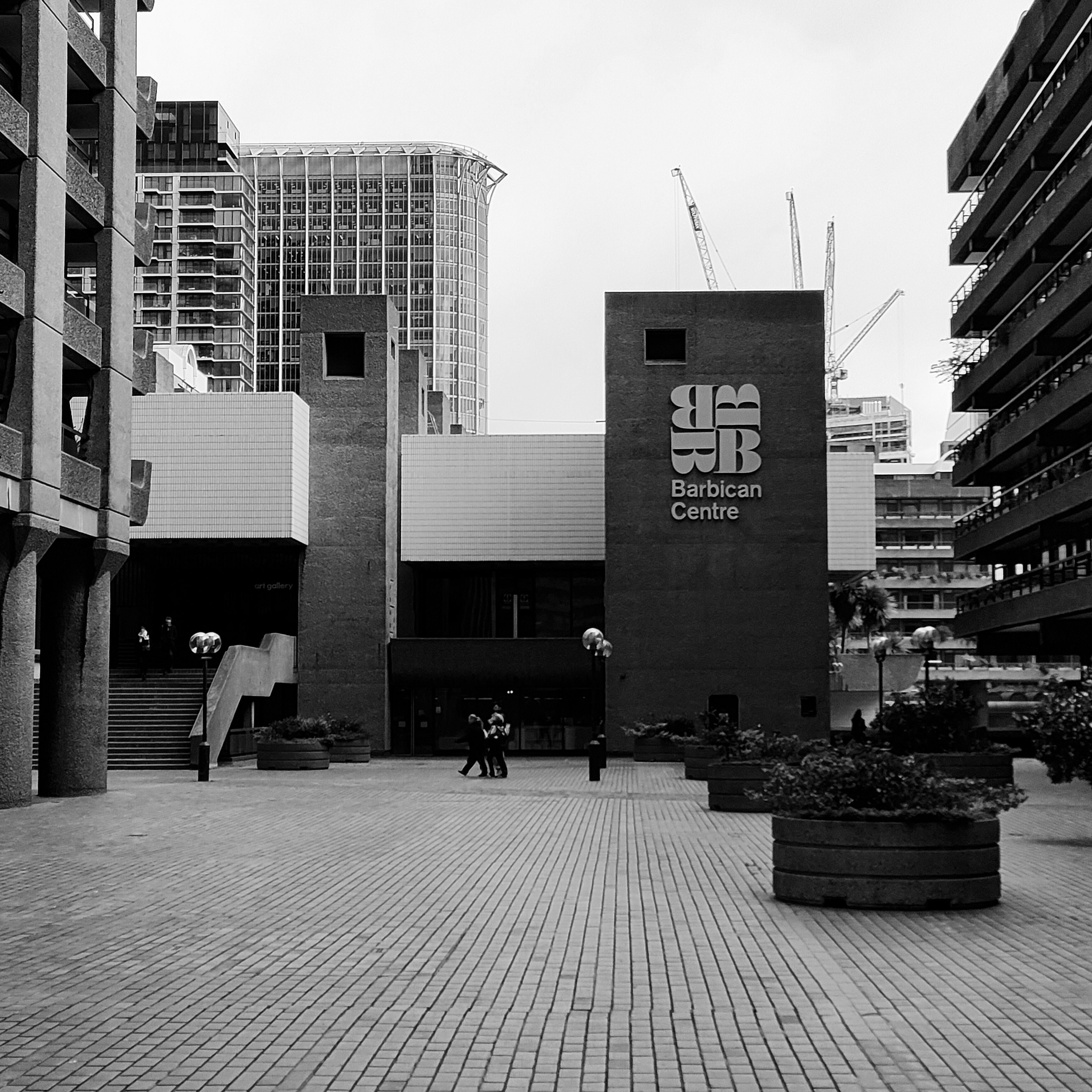 A Grayscale Photo of People Walking on Sidewalk Near Building