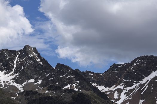 Scenic view of snow-capped rocky mountains beneath a cloudy sky, showcasing raw natural beauty.