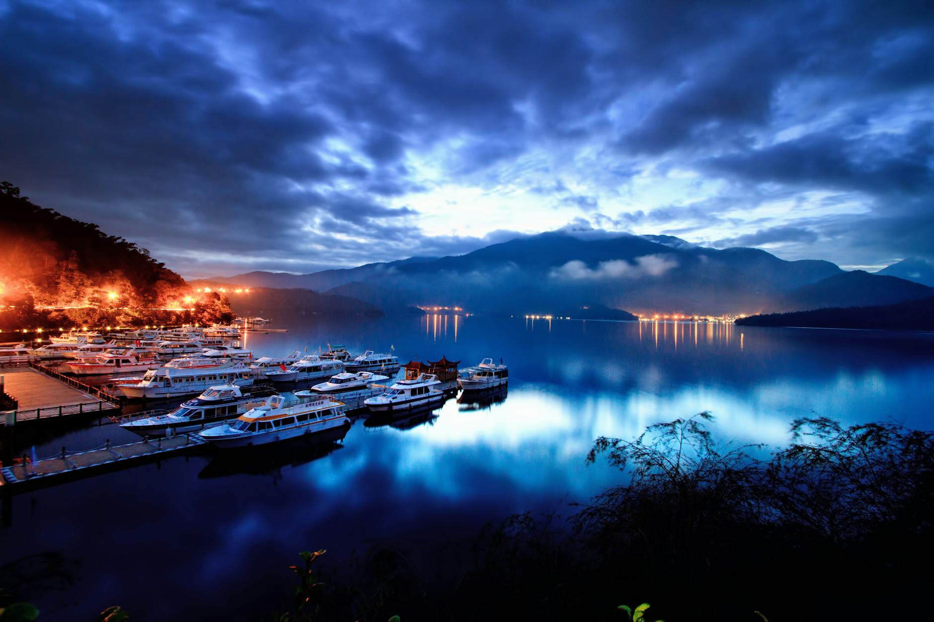 Tranquil evening at Sun Moon Lake with boats docked, surrounded by misty mountains