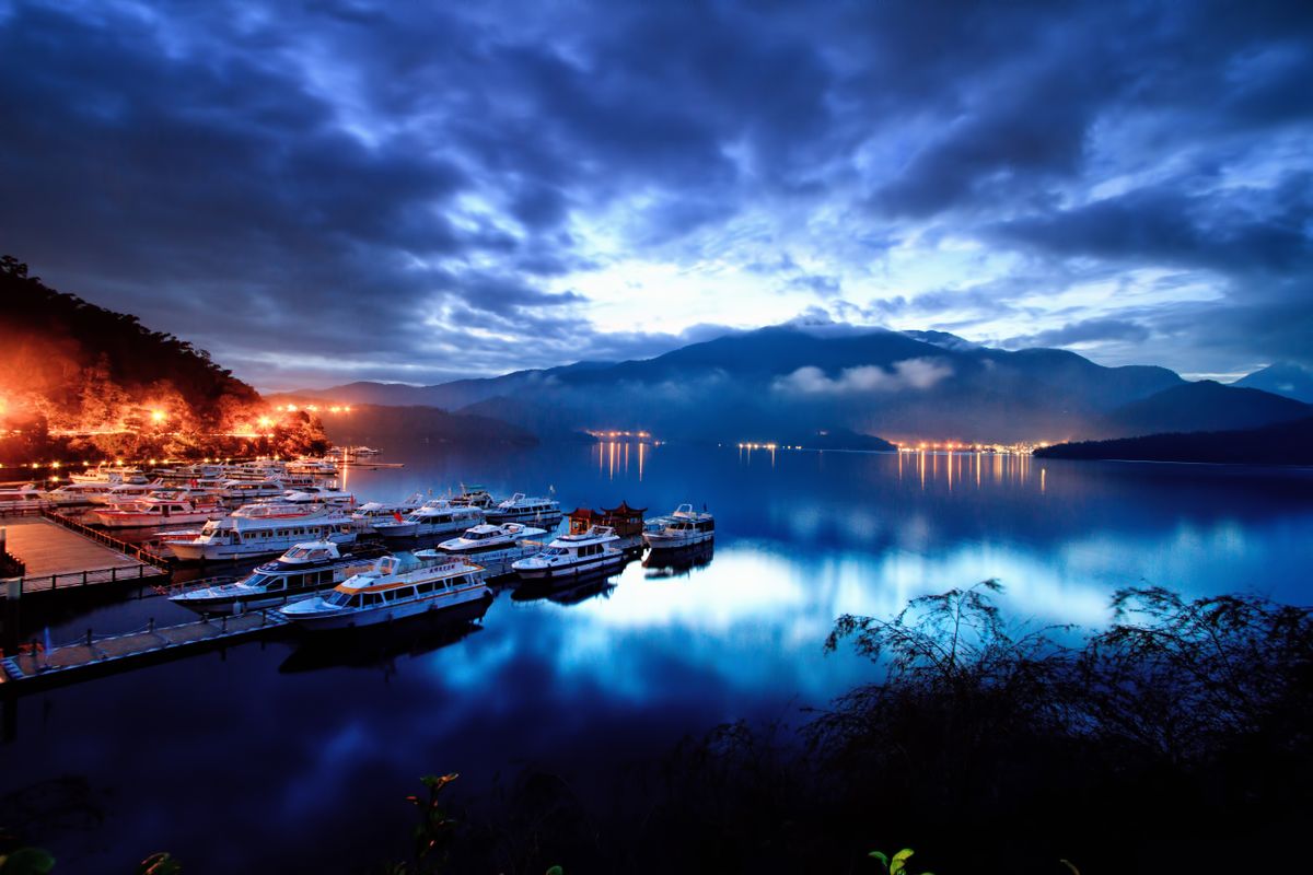 Boats moored at a Sun Moon Lake pier at dusk with mountains reflected in the water